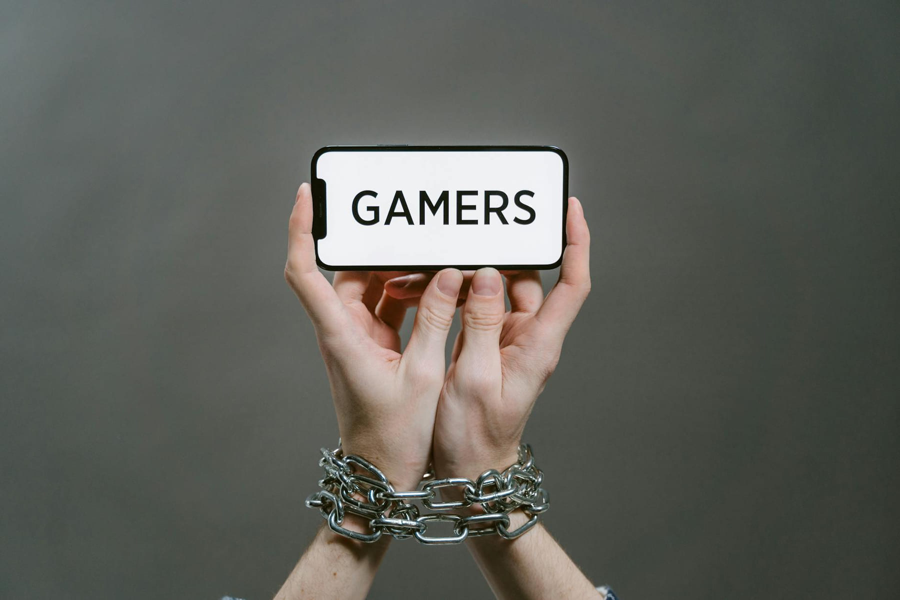 Conceptual image of a person holding a smartphone labeled 'GAMERS' with chained hands. on Quest on Chain