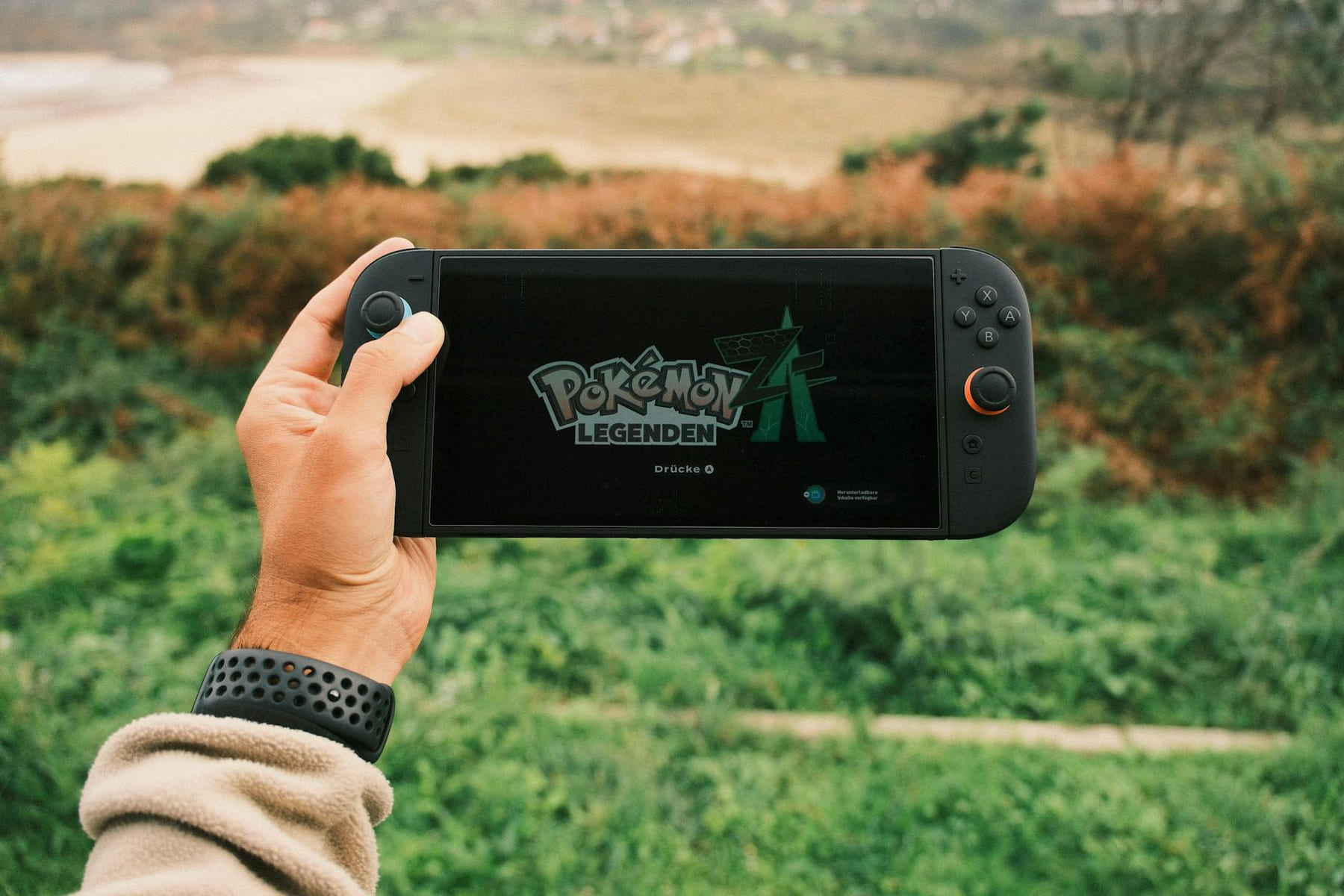 A person holds a handheld gaming device outdoors with Pokémon Legends on screen. on Quest on Chain