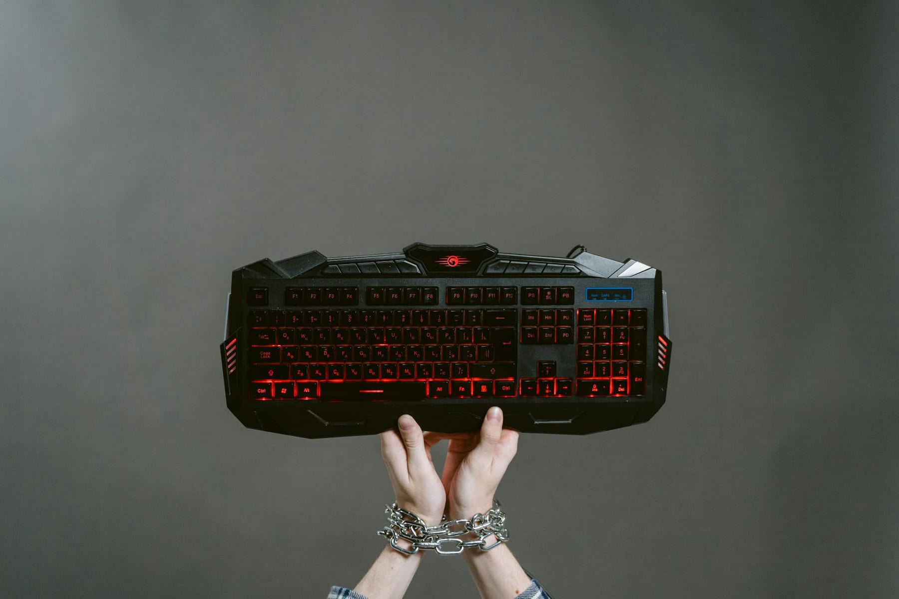 Hands bound by chains holding a mechanical gaming keyboard with red backlight. on Quest on Chain