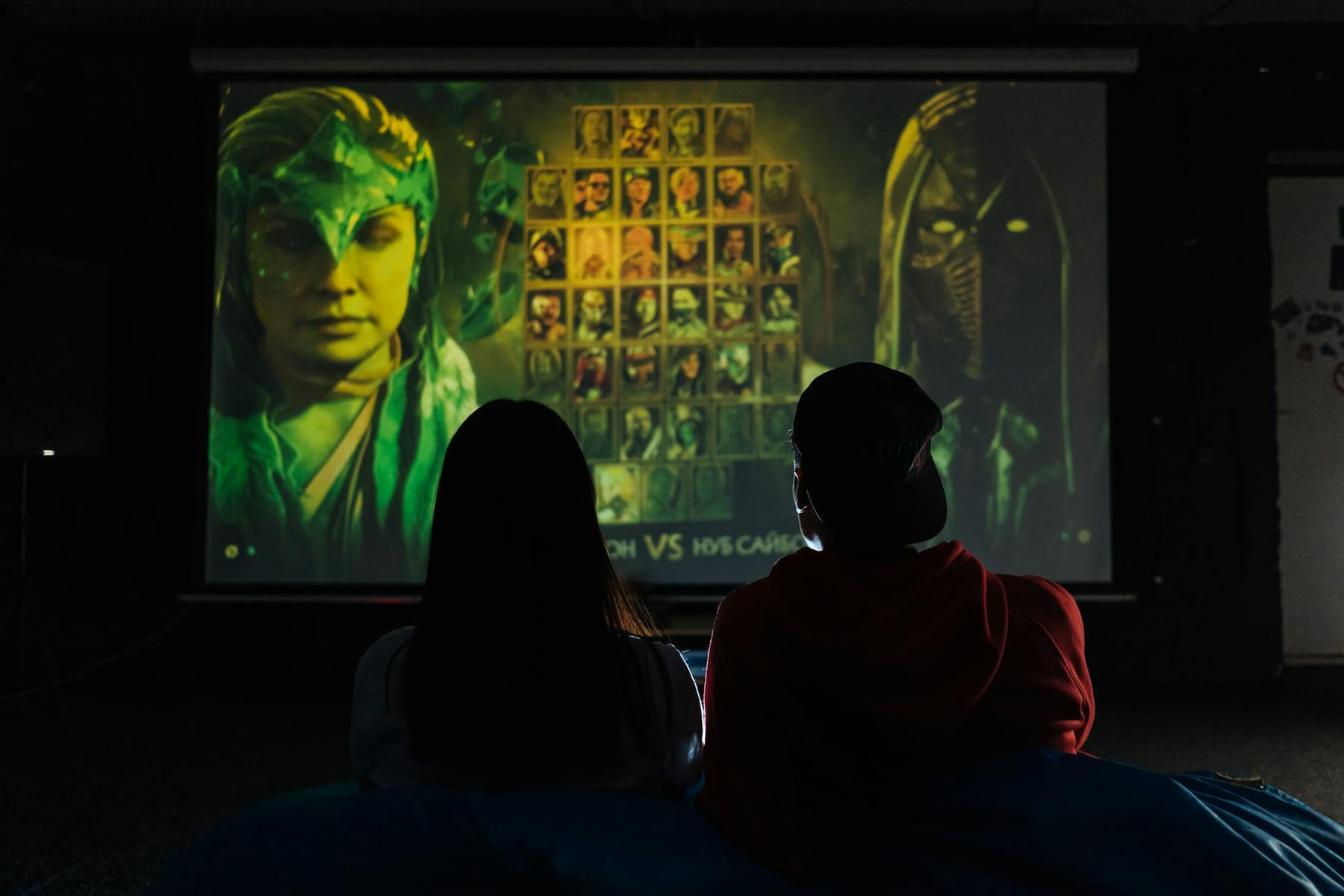 Two people sitting indoors gaming on a large projector screen, enjoying a video game session. on Quest on Chain
