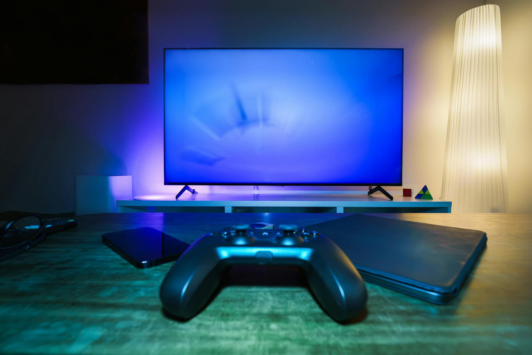 A stylish and ambient gaming setup featuring a controller, smart devices, and a TV in a lit living room. on Quest on Chain